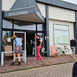 Winkelgevel van Kringloopwinkel met donker frame, witte pui en entree, zithoeken en fiets op het terras