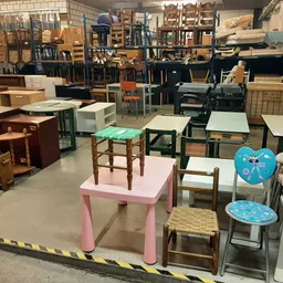 Diverse meubels en stoelen uitgestald in kringloopwinkel, waaronder roze tafel, houten stoelen en kinderstoelen