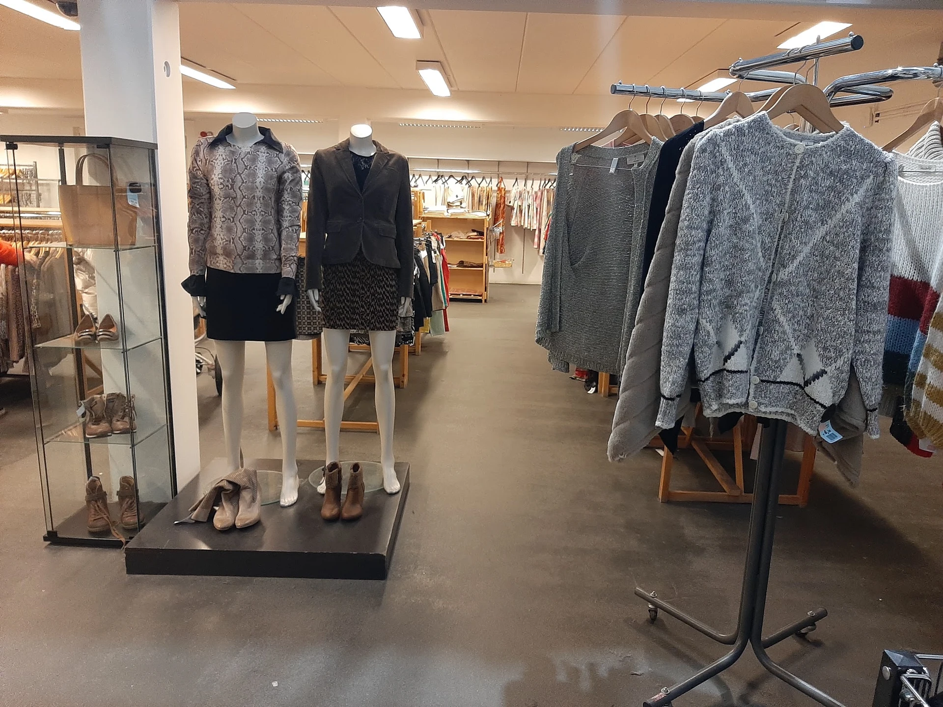 Rekken met tweedehands dameskleding, waaronder truien, jassen en jurken op hangers in de winkel