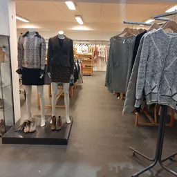 Rekken met tweedehands dameskleding, waaronder truien, jassen en jurken op hangers in de winkel