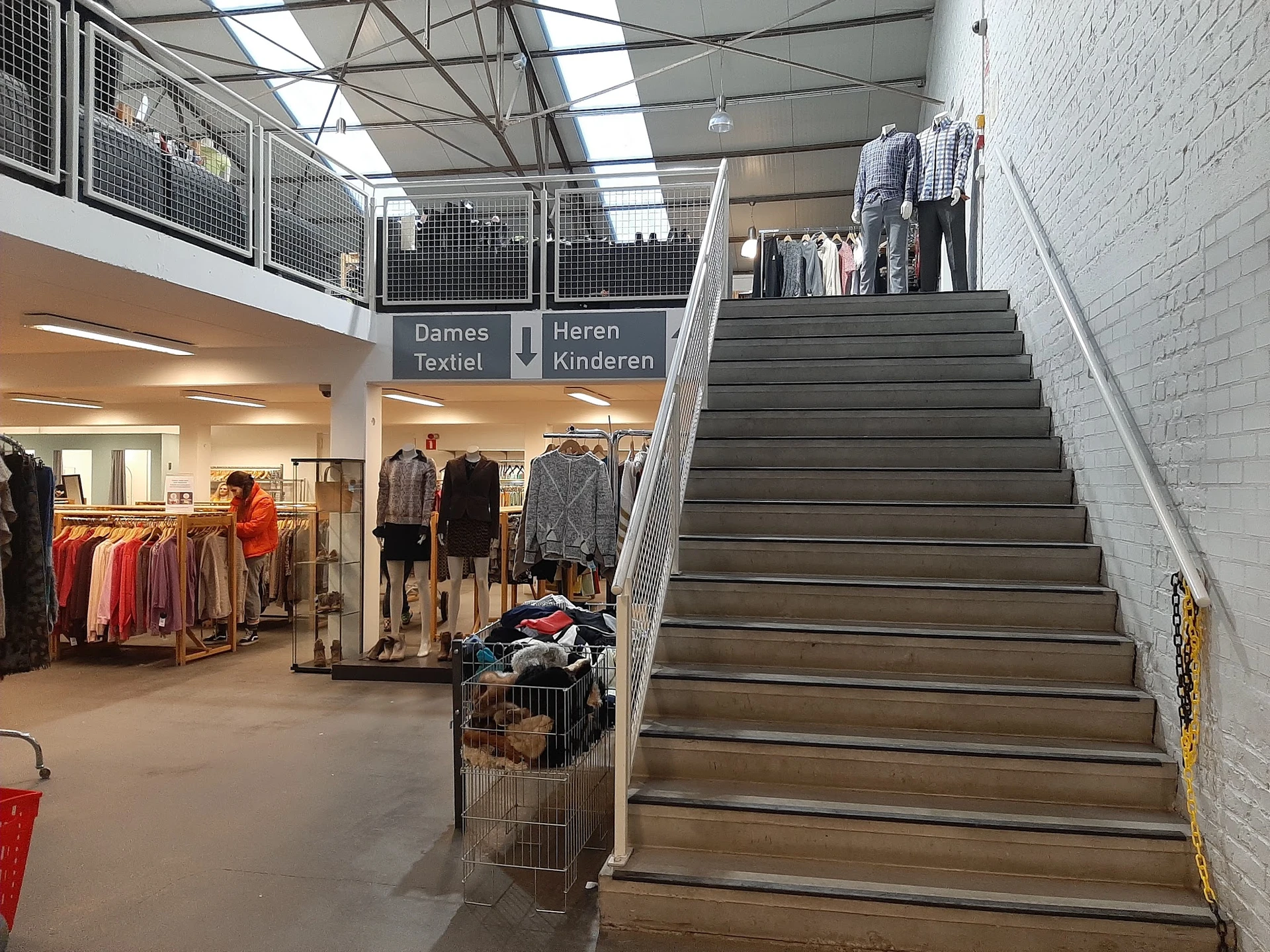 Winkelinterieur met trappen, dameskleding en kinderkleding afdelingen, stellingen met kleding