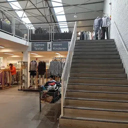 Winkelinterieur met trappen, dameskleding en kinderkleding afdelingen, stellingen met kleding