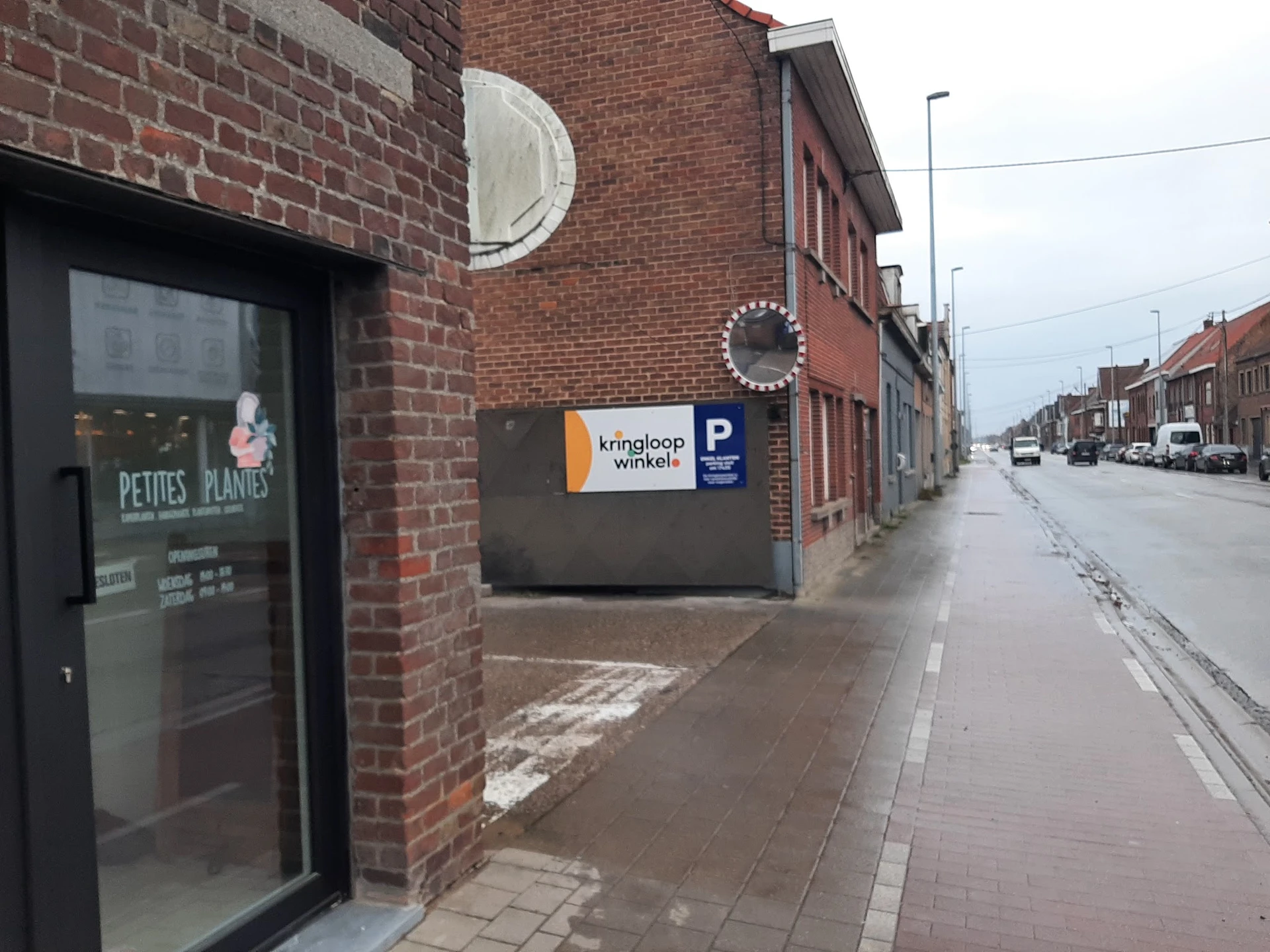 Bakstenen gevel van kringloopwinkel met ingang, ronde ramen en bord met logo