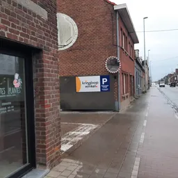 Bakstenen gevel van kringloopwinkel met ingang, ronde ramen en bord met logo