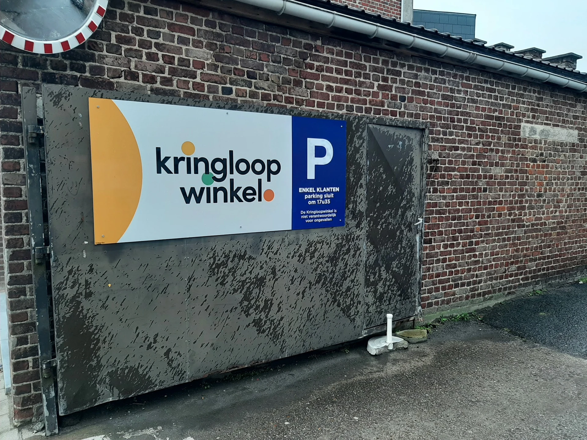 Grijze gevel met wit en blauw bord met logo en parkeerplaats-pictogram