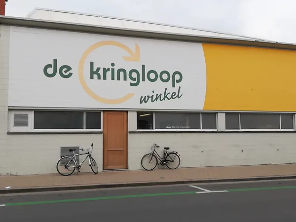 Witte gevel van kringloopwinkel met geel accent en twee fietsen ervoor