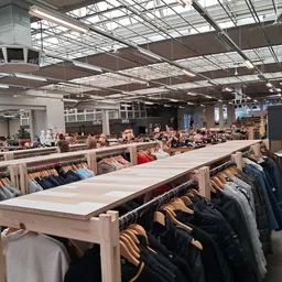 Ruim winkelinterieur met houten kledingrekken vol tweedehands kleding, industrieel plafond met daglicht