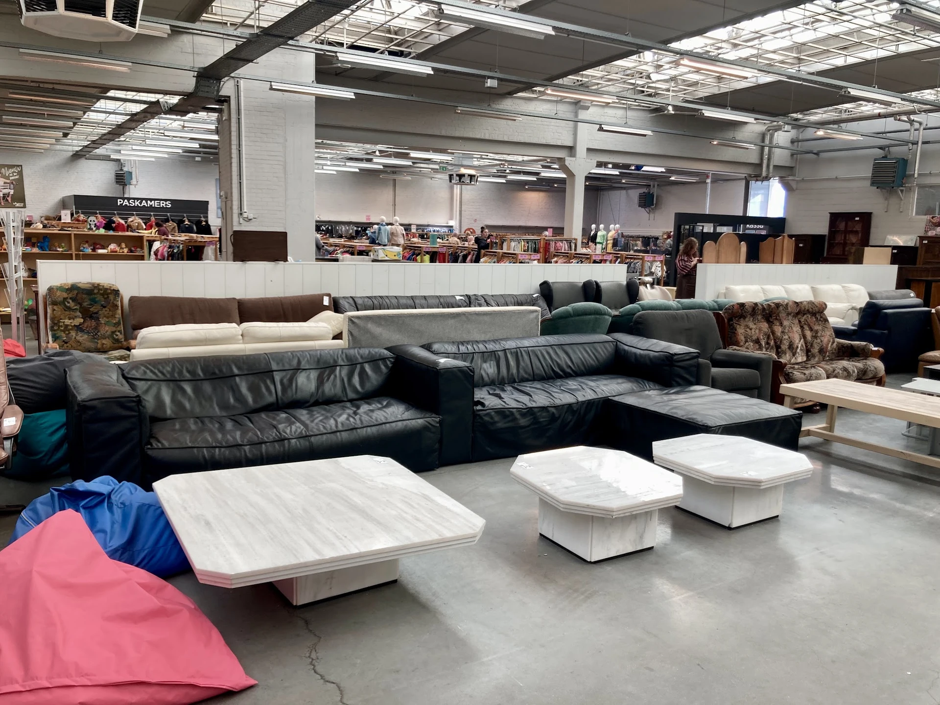 Uitgestalde tweedehands meubels in een kringloopwinkel, waaronder zwarte leren banken en witte poefjes