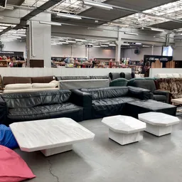 Uitgestalde tweedehands meubels in een kringloopwinkel, waaronder zwarte leren banken en witte poefjes