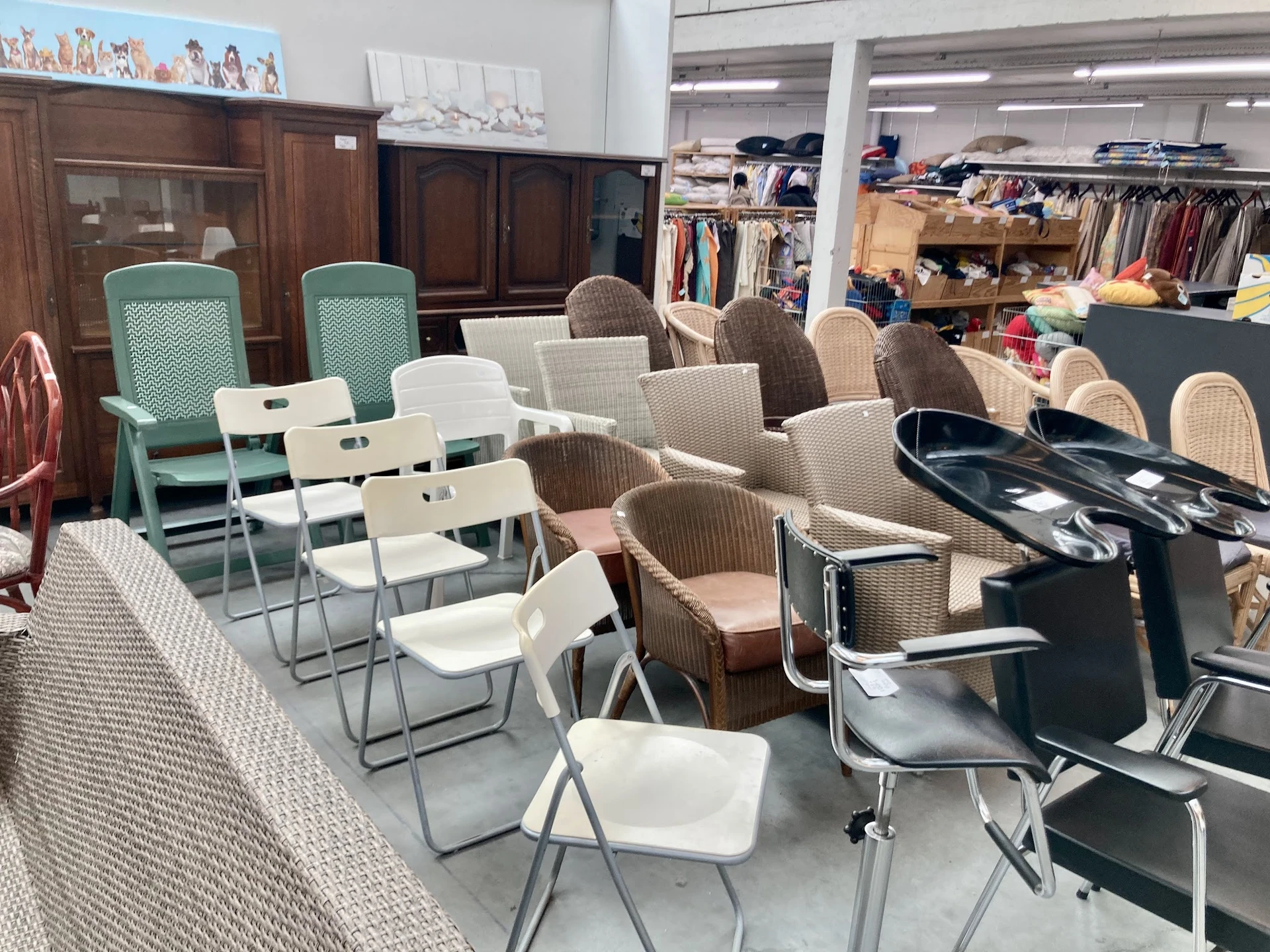 Zithoek met diverse stoelen en tafels in kringloopwinkel, op achtergrond kleding en meubels