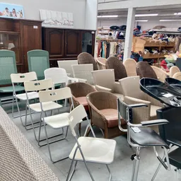 Zithoek met diverse stoelen en tafels in kringloopwinkel, op achtergrond kleding en meubels