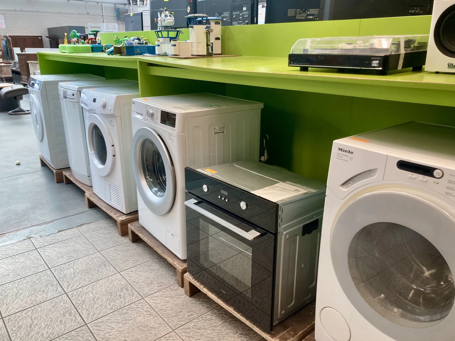 Uitgestalde wasmachines, drogers en een oven op palletten in de winkel