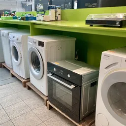 Uitgestalde wasmachines, drogers en een oven op palletten in de winkel