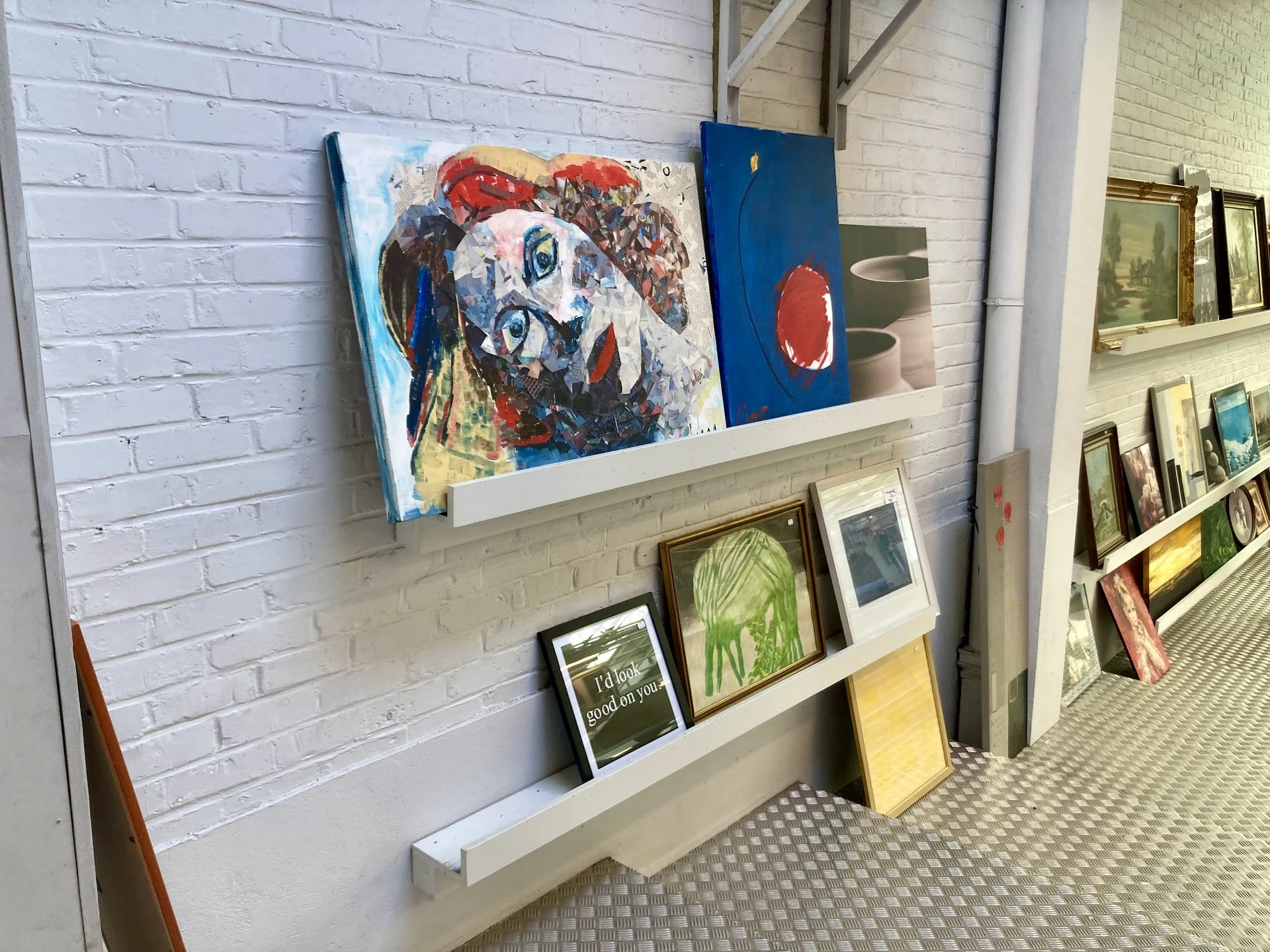 Wandplankjes met kunstwerken, schilderijen en decoratieve items in een kringloopwinkel