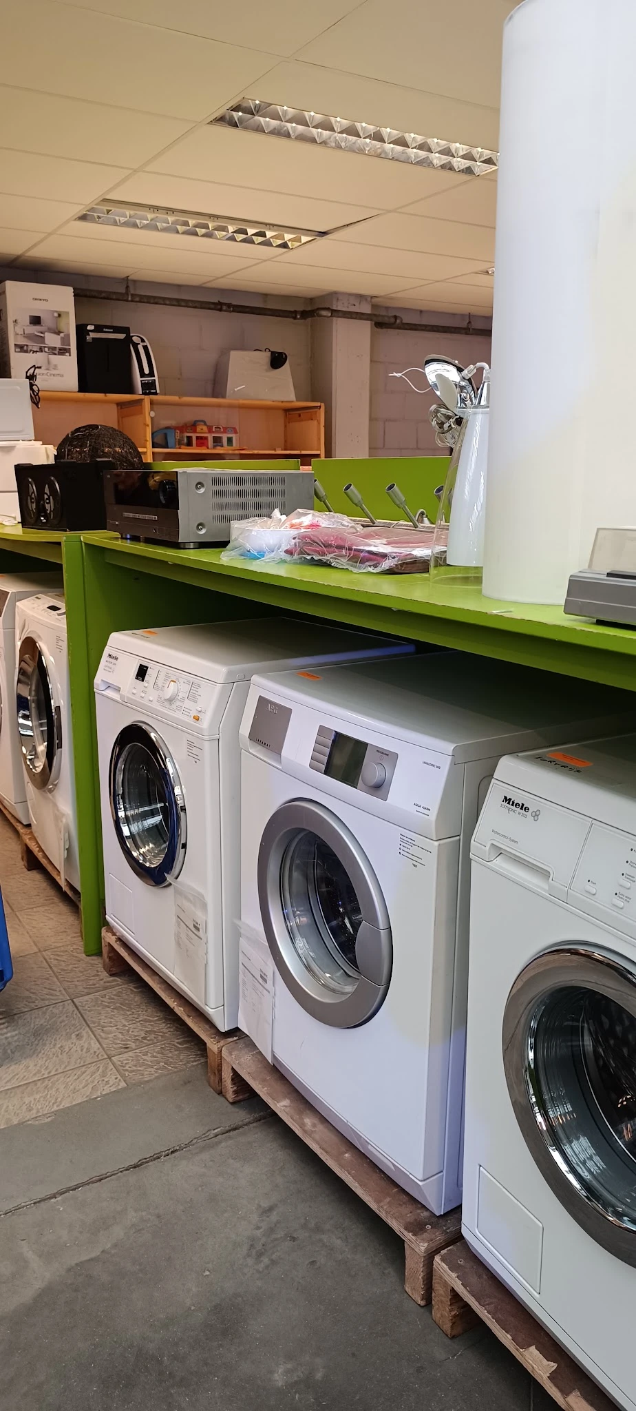 Witgoedafdeling met verschillende wasmachines en droogkasten onder groen stellingwerk