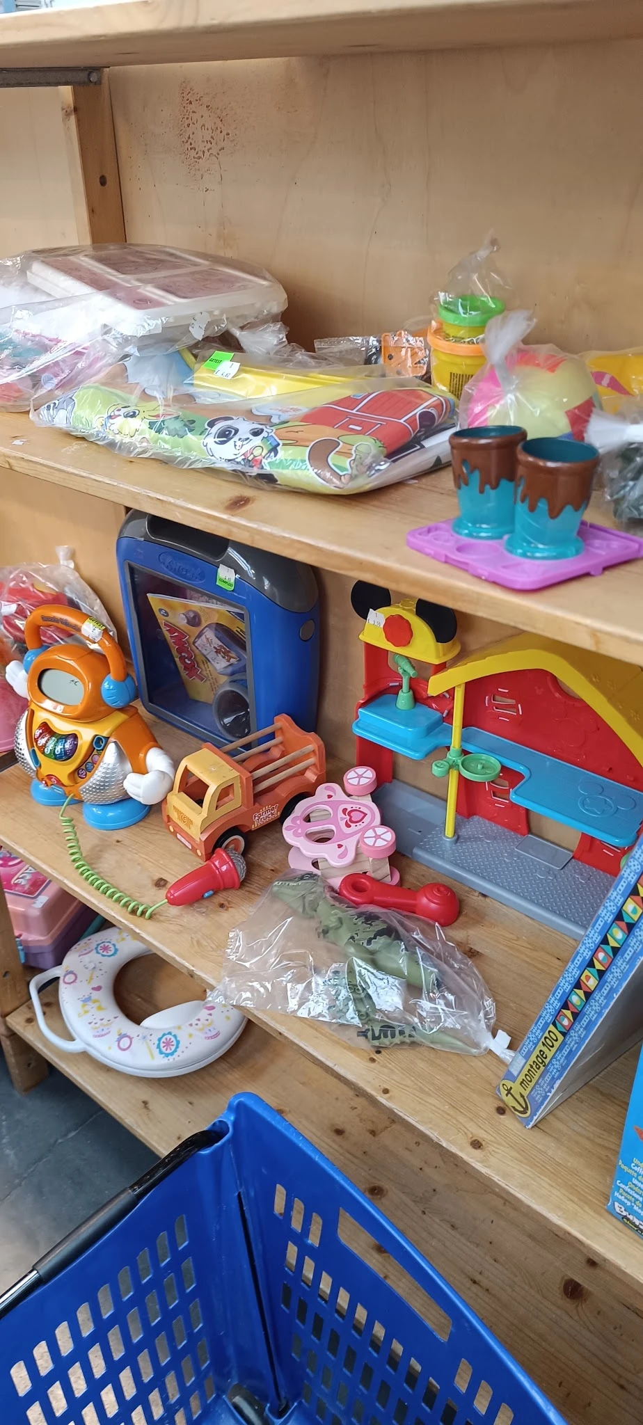 Speelgoed en kinderartikelen op een houten plank, waaronder een oranje speeltje, een blauwe radio, een rode vrachtwagen en ee