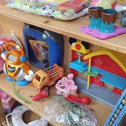 Speelgoed en kinderartikelen op een houten plank, waaronder een oranje speeltje, een blauwe radio, een rode vrachtwagen en ee