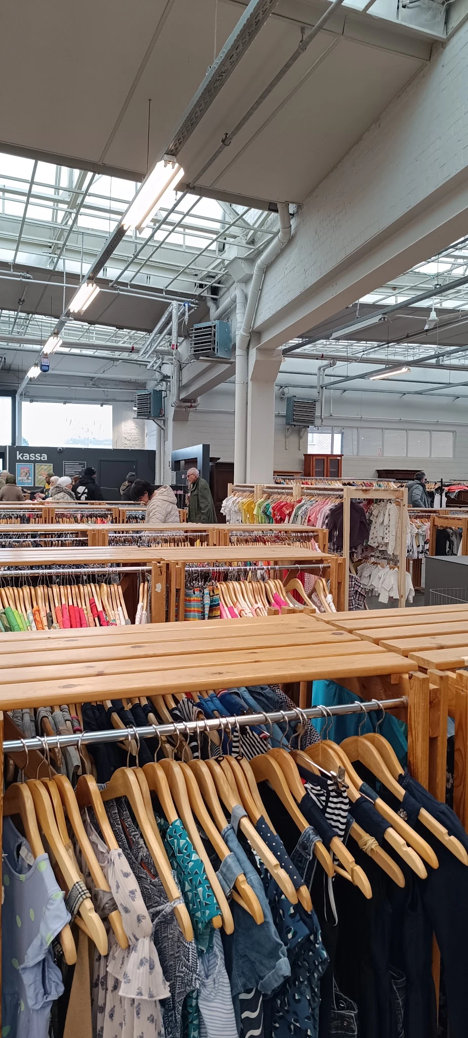 Houten rekken met kleding, boeken en andere tweedehandsartikelen in de kringloopwinkel