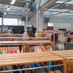 Houten rekken met kleding, boeken en andere tweedehandsartikelen in de kringloopwinkel
