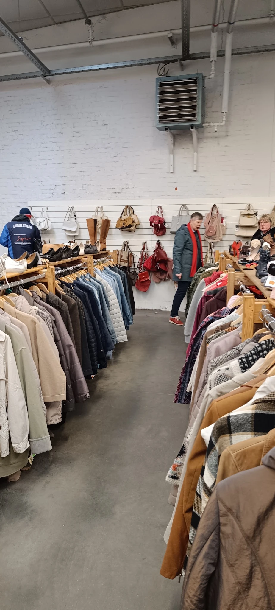 Winkelinterieur met kledingrekken, tassen en accessoires aan muren, bezoekers aan het winkelen