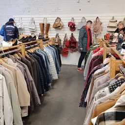 Winkelinterieur met kledingrekken, tassen en accessoires aan muren, bezoekers aan het winkelen