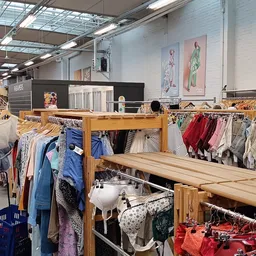 Houten rekken met tweedehands kleding, kinderkleding en textiel netjes uitgestald in de winkel