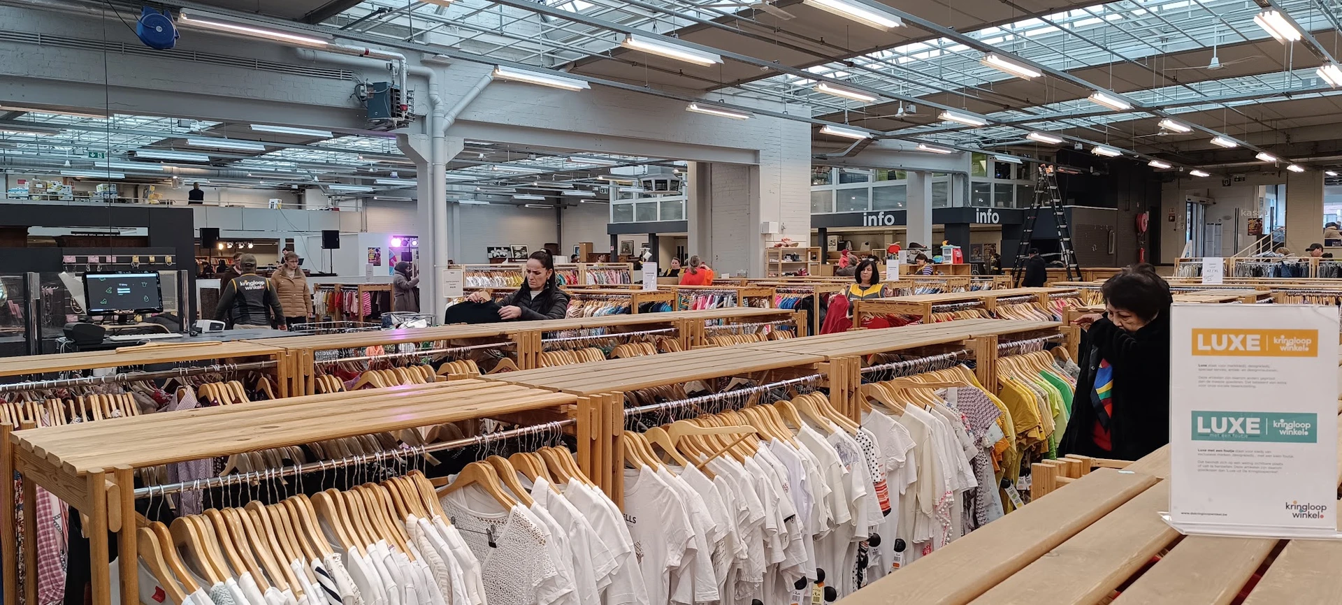 Rekken met witte en gekleurde kledingstukken op houten hangers in een kringloopwinkel