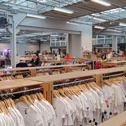 Rekken met witte en gekleurde kledingstukken op houten hangers in een kringloopwinkel