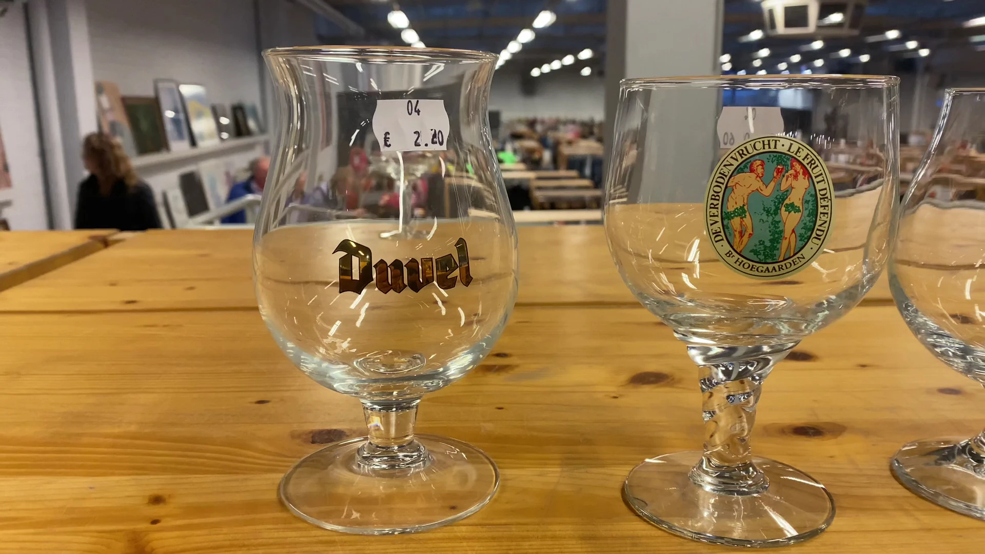 Twee bierglazen op houten tafel, links een Duvel-glas met prijskaartje, rechts een groen logo-glas