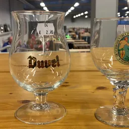 Twee bierglazen op houten tafel, links een Duvel-glas met prijskaartje, rechts een groen logo-glas