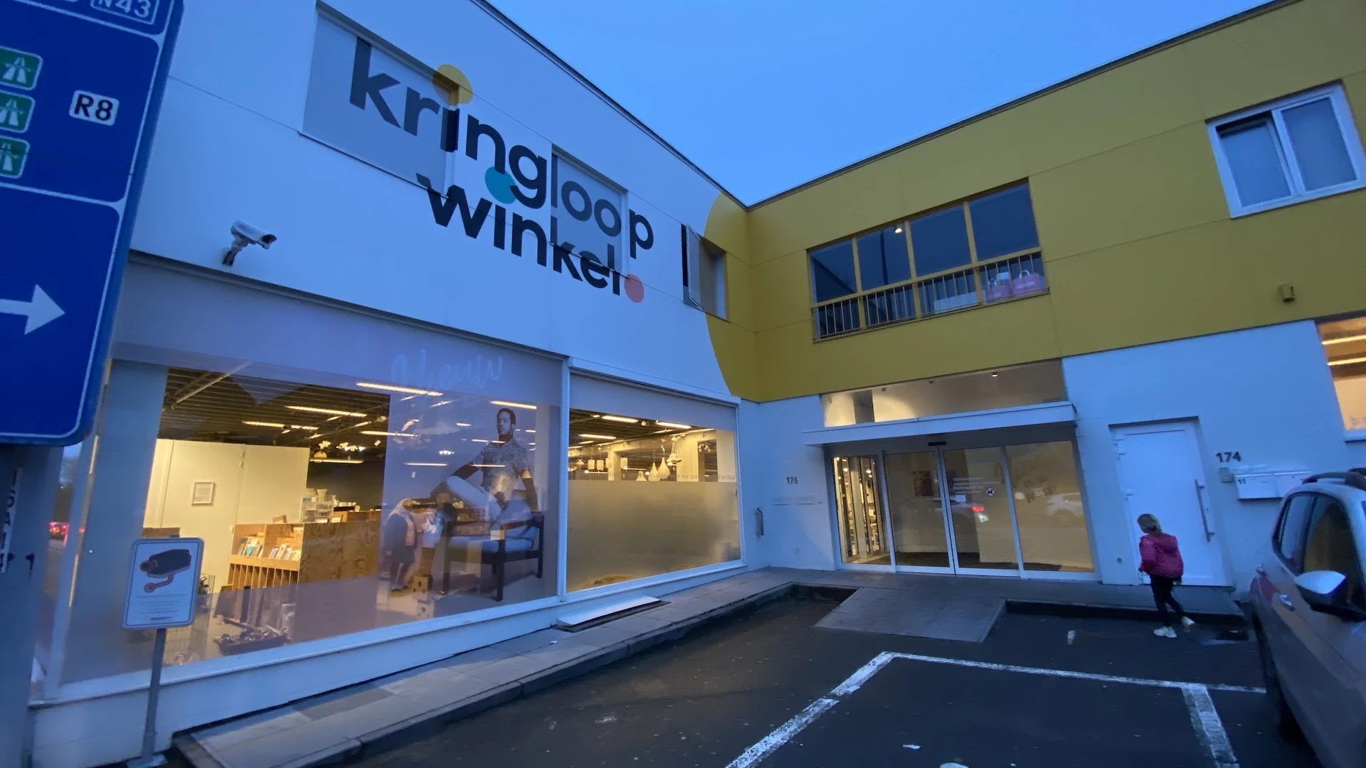Gevel van kringloopwinkel met blauwe en gele gevelbekleding, grote ramen en duidelijk zichtbare winkelnaam