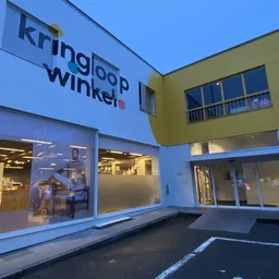 Gevel van kringloopwinkel met blauwe en gele gevelbekleding, grote ramen en duidelijk zichtbare winkelnaam