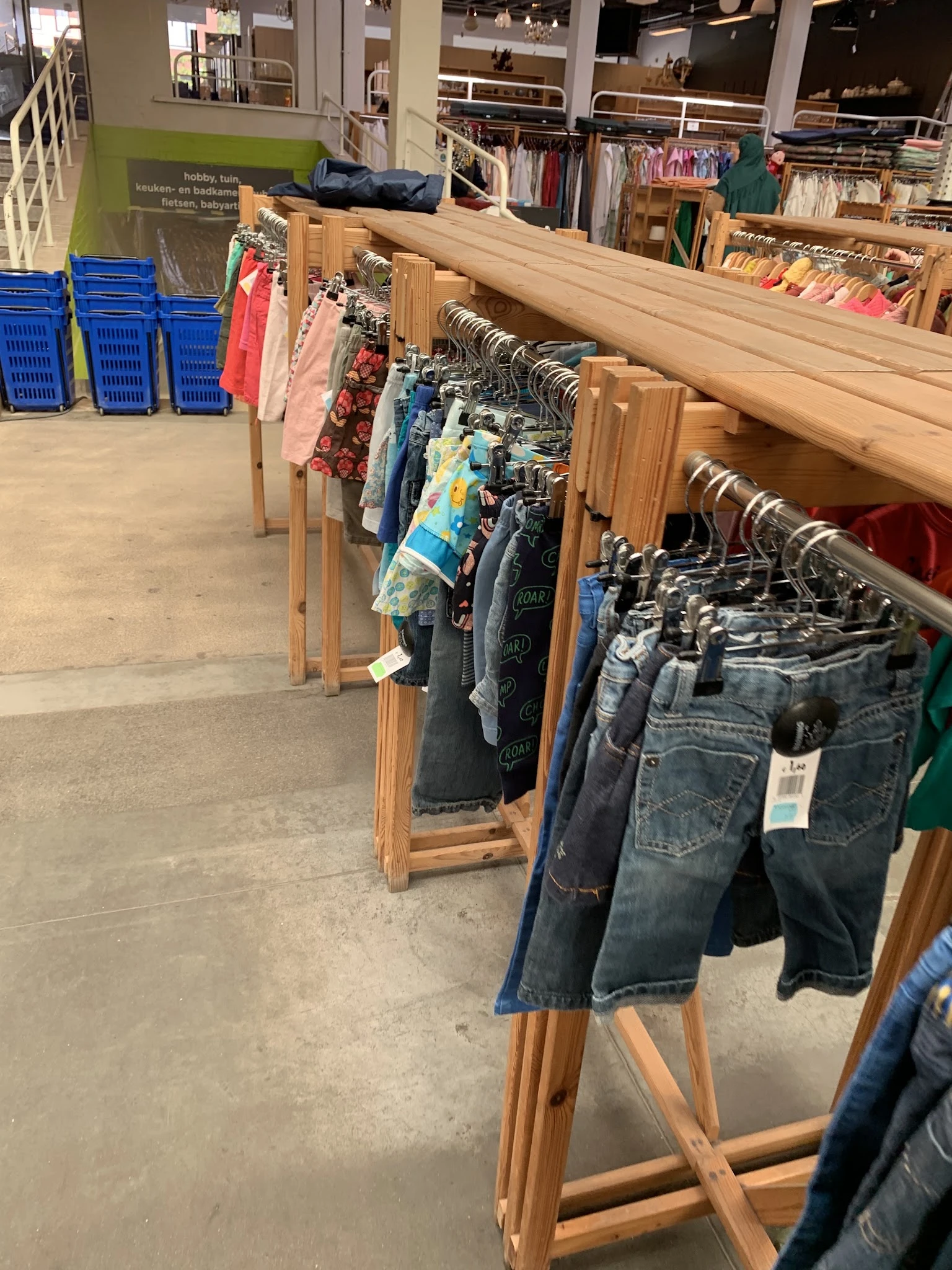 Rekken met tweedehands kleding: jeans, shirts en jurken op hangers in de kringloopwinkel