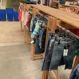 Rekken met tweedehands kleding: jeans, shirts en jurken op hangers in de kringloopwinkel