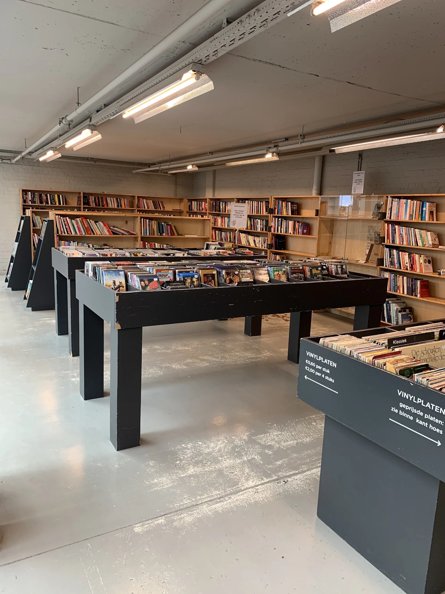 Winkelvloer met zwarte tafels met boeken en vinyl's, boekenkasten aan de muur, fluorescente verlichting