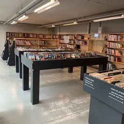 Winkelvloer met zwarte tafels met boeken en vinyl's, boekenkasten aan de muur, fluorescente verlichting