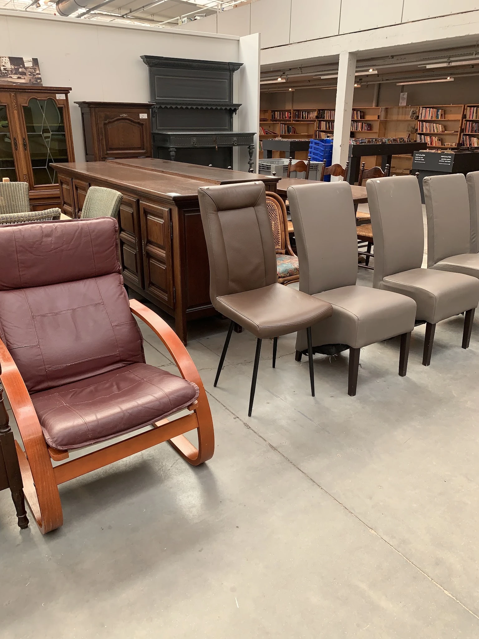 Groep grijze stoelen en een bruinrode fauteuil met houten frame in showroom