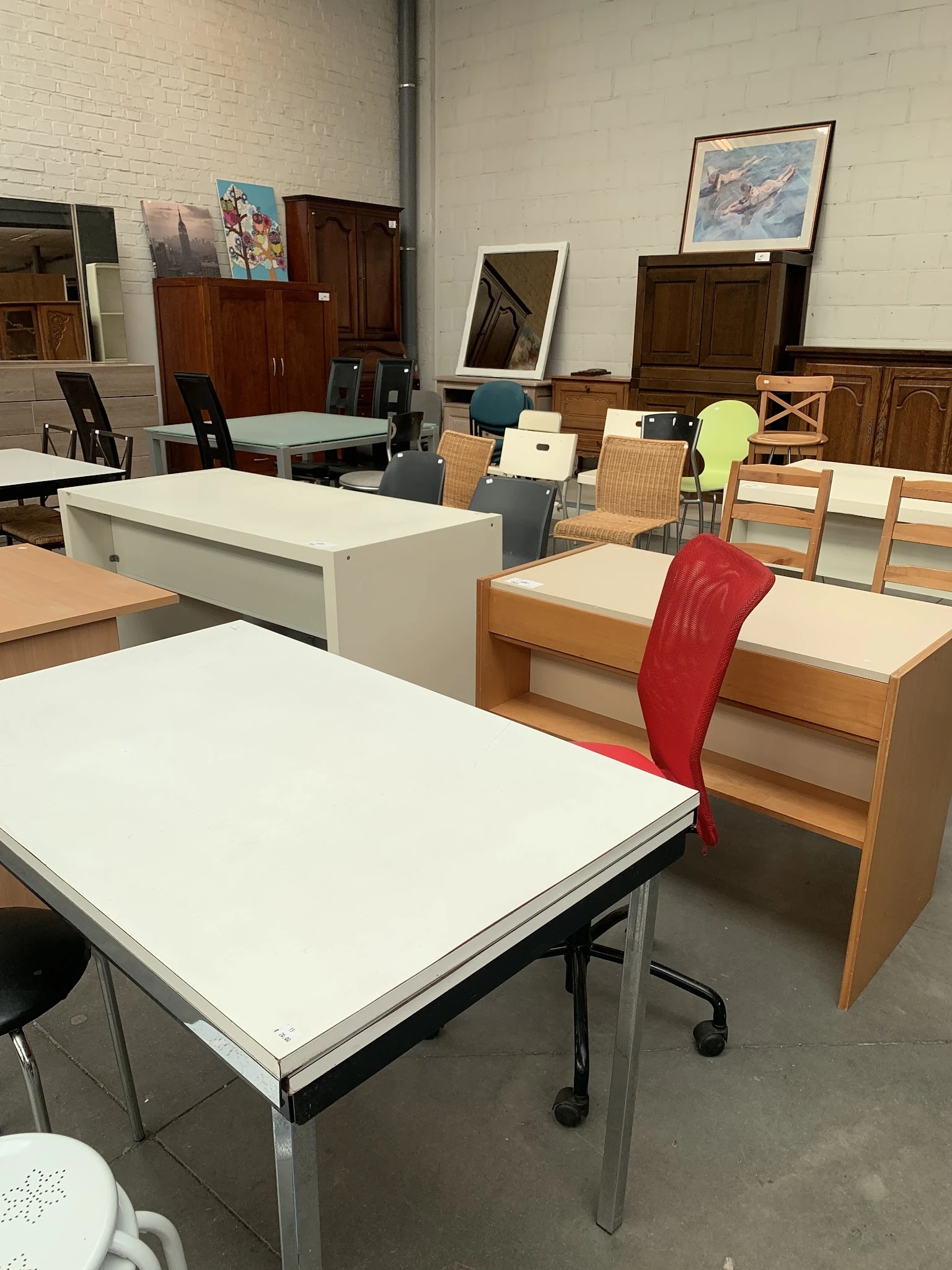 Winkelvloer met diverse meubels: witte en houten tafels, stoelen in verschillende kleuren, en kastjes.