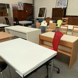 Winkelvloer met diverse meubels: witte en houten tafels, stoelen in verschillende kleuren, en kastjes.
