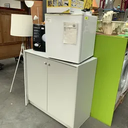 Uitgestalde meubels in de winkel: witte kast met deuren, witte lamp en groene kasten op de achtergrond