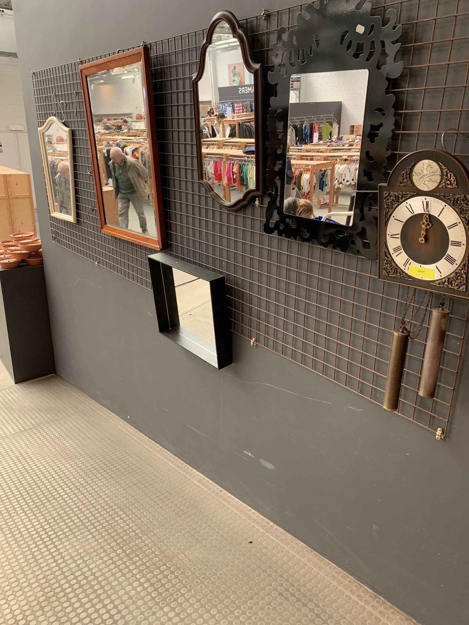 Winkelinterieur met grijze muur, zwarte tegeltjes, wandklok, spiegel en enkele decoratieve items