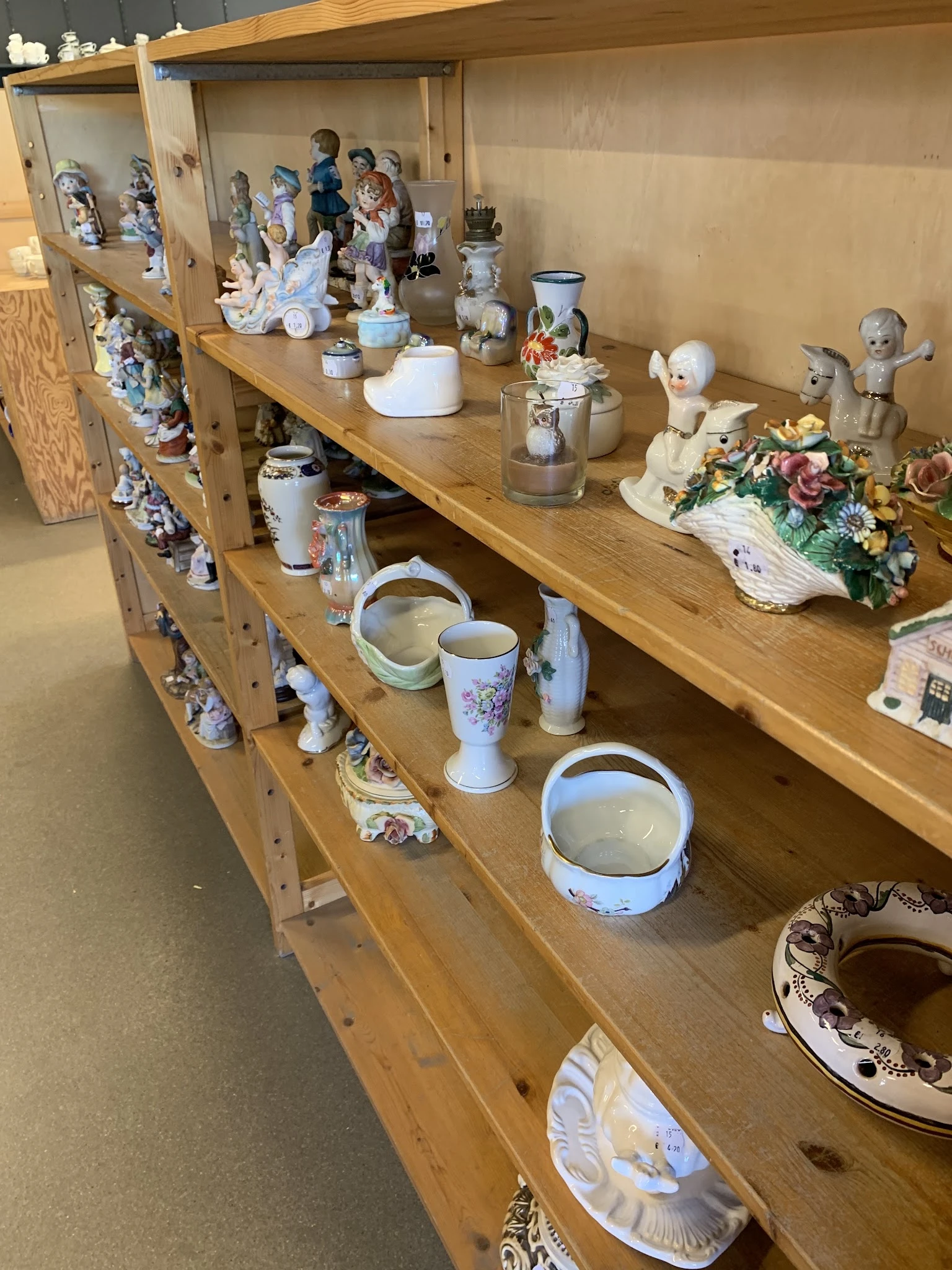 Houten stellingen met decoratieve items: porseleinen beeldjes, vazen, schalen en bloemarrangementen