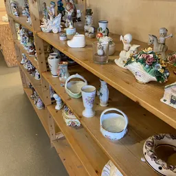 Houten stellingen met decoratieve items: porseleinen beeldjes, vazen, schalen en bloemarrangementen