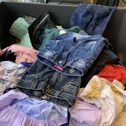 Stapel tweedehands kleding met jeans, shirts en andere kledingstukken in verschillende kleuren