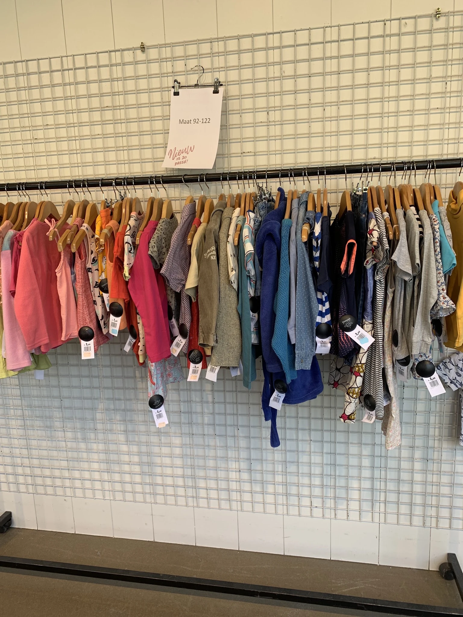Kledingrek met diverse tweedehands kleding op houten hangers, gesorteerd op kleur