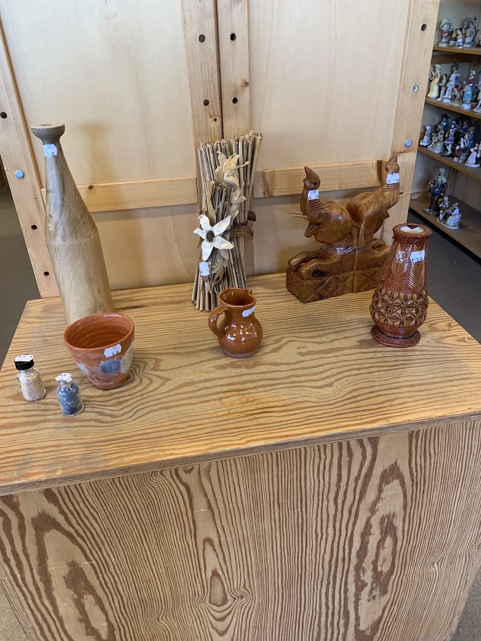 Uitgestalde decoratieve artikelen op een houten tafel: keramische potten, houten beeldjes, vazen en kleine flesjes