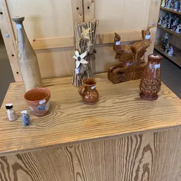 Uitgestalde decoratieve artikelen op een houten tafel: keramische potten, houten beeldjes, vazen en kleine flesjes