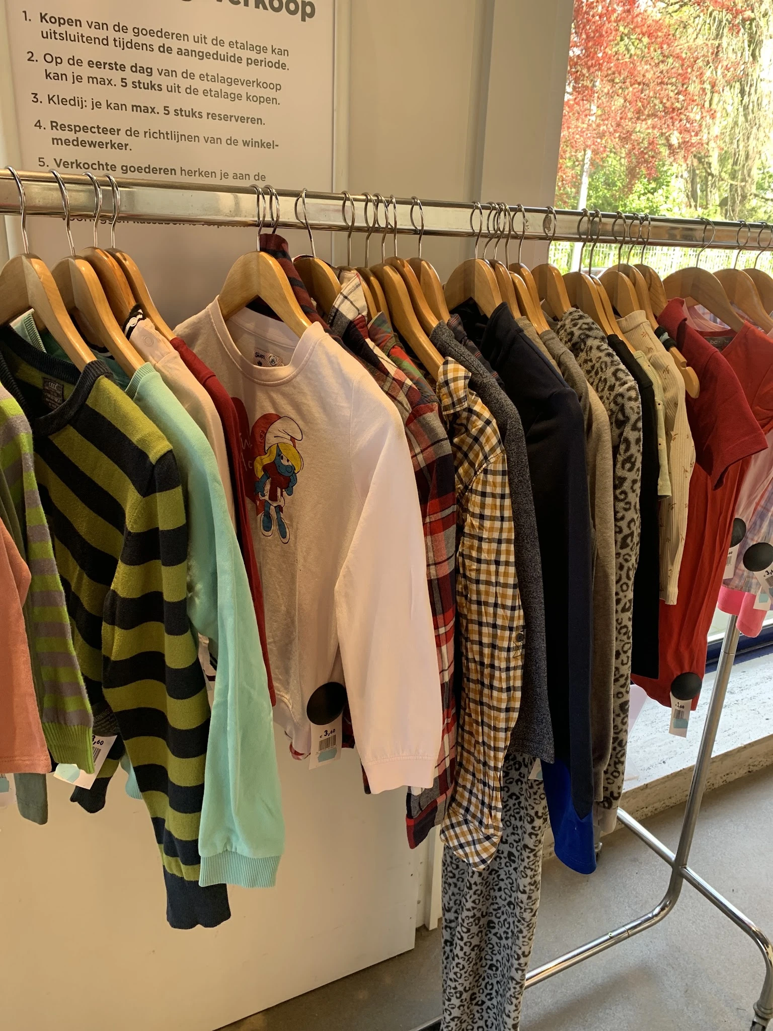 Rekken met tweedehands kleding op hangers, waaronder gestreepte truien, shirts met prints, geruite blouses en jurkjes in vers