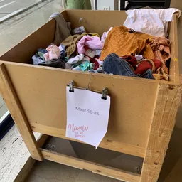 Grote kartonnen doos vol tweedehands kleding, met prijskaartje 'Maat 50-86' eraan bevestigd
