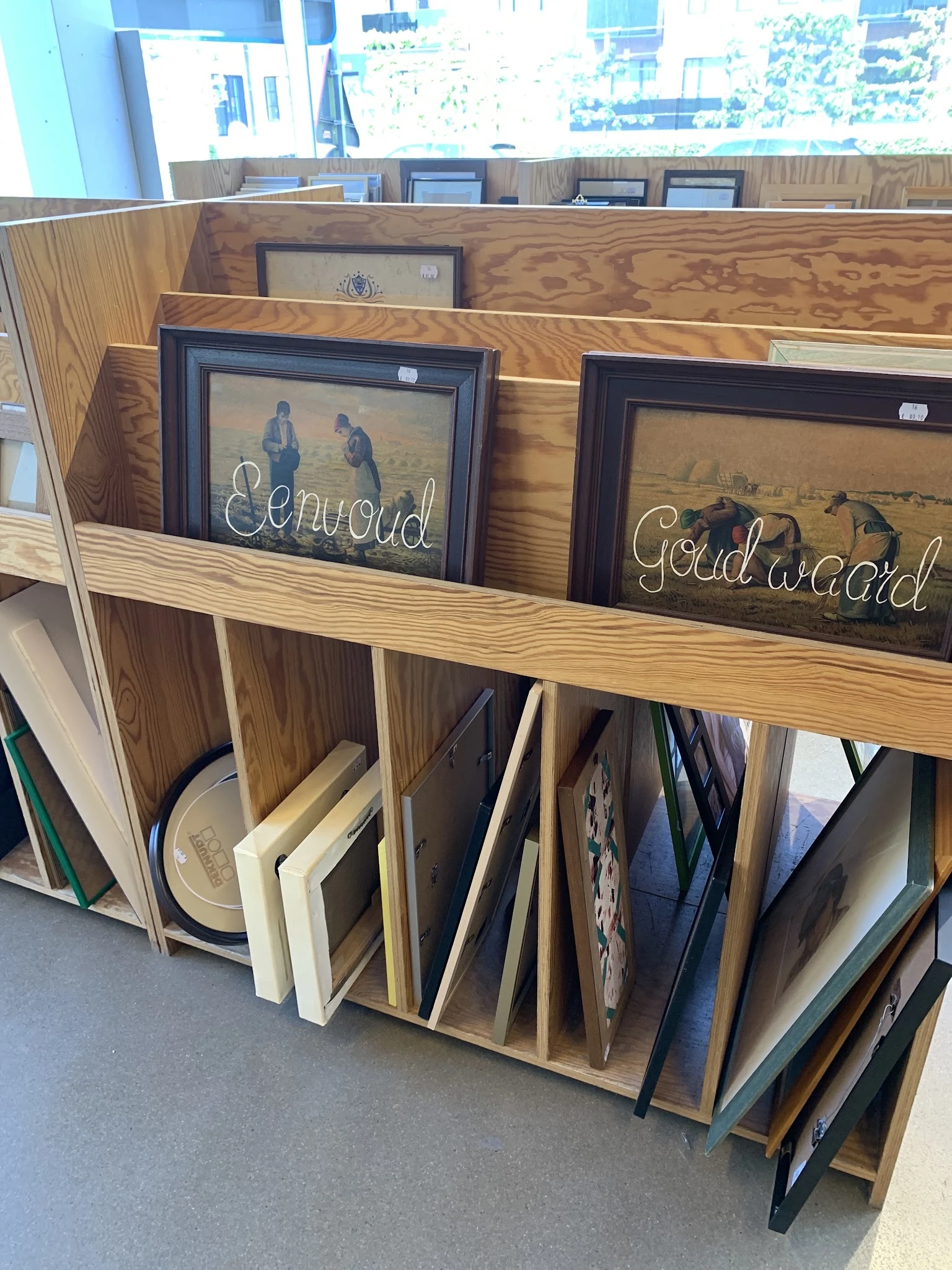 Uitgestalde tweedehands schilderijen en kunstwerken op een houten rek in de winkel
